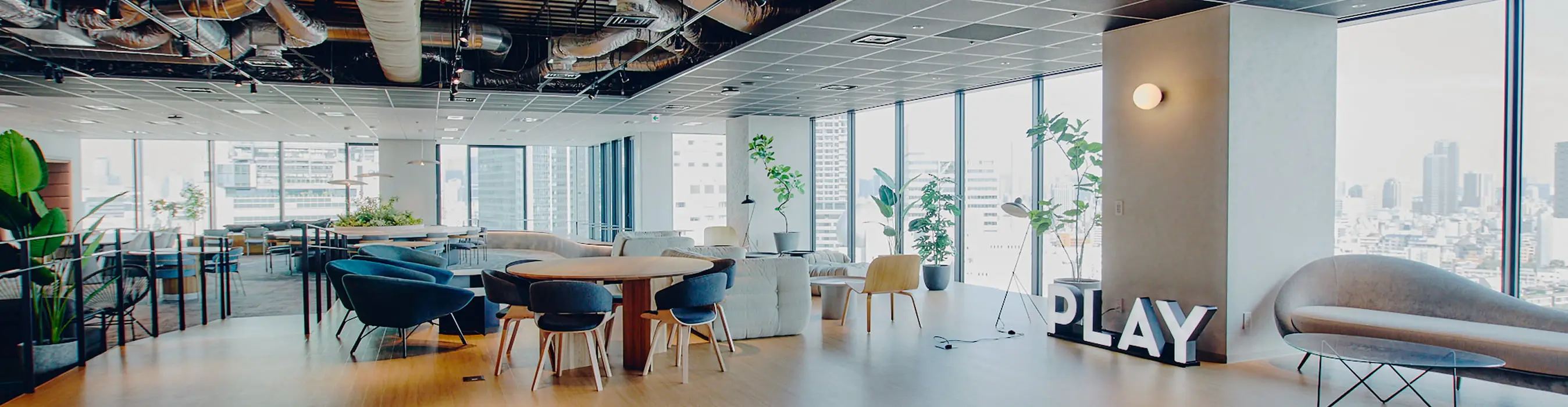 モダンで広々としたオフィス空間に、様々なタイプの座席や大きな窓、そして「PLAY」の文字が配置されている様子
