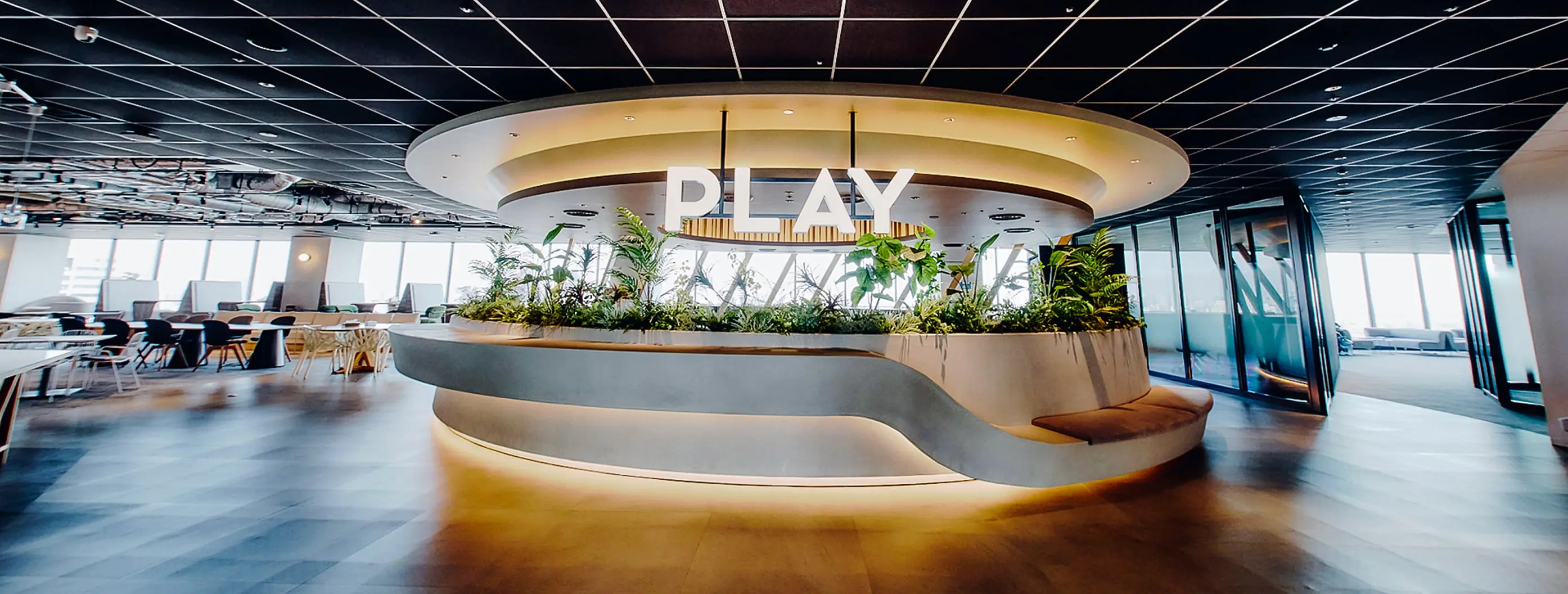 「PLAY」の文字が飾られた、植物が豊かな曲線状のカウンターと、奥に広がるモダンなラウンジ空間