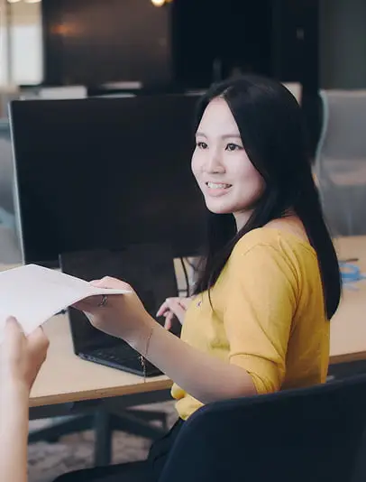 モダンなオフィスで、笑顔の若い女性が同僚から書類を受け取っている様子