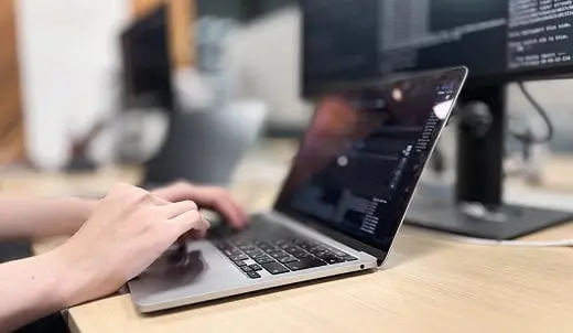 モダンなオフィスで、ノートパソコンのキーボードを操作し、画面にコードを表示して作業する手元