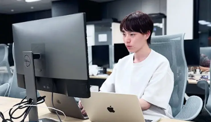 モダンなオフィスで、複数のコンピューターを使って集中して作業する若いエンジニア