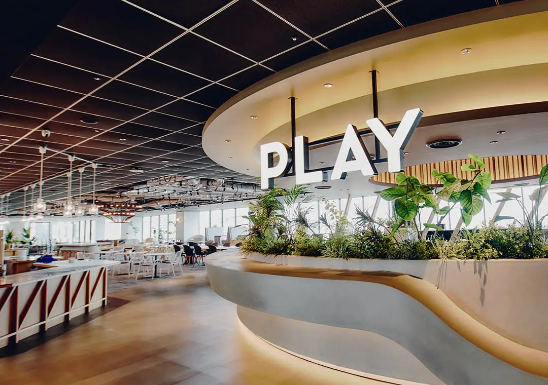 「PLAY」の文字が飾られた、植物が豊かな曲線状のカウンターと、奥に広がるモダンなラウンジ空間