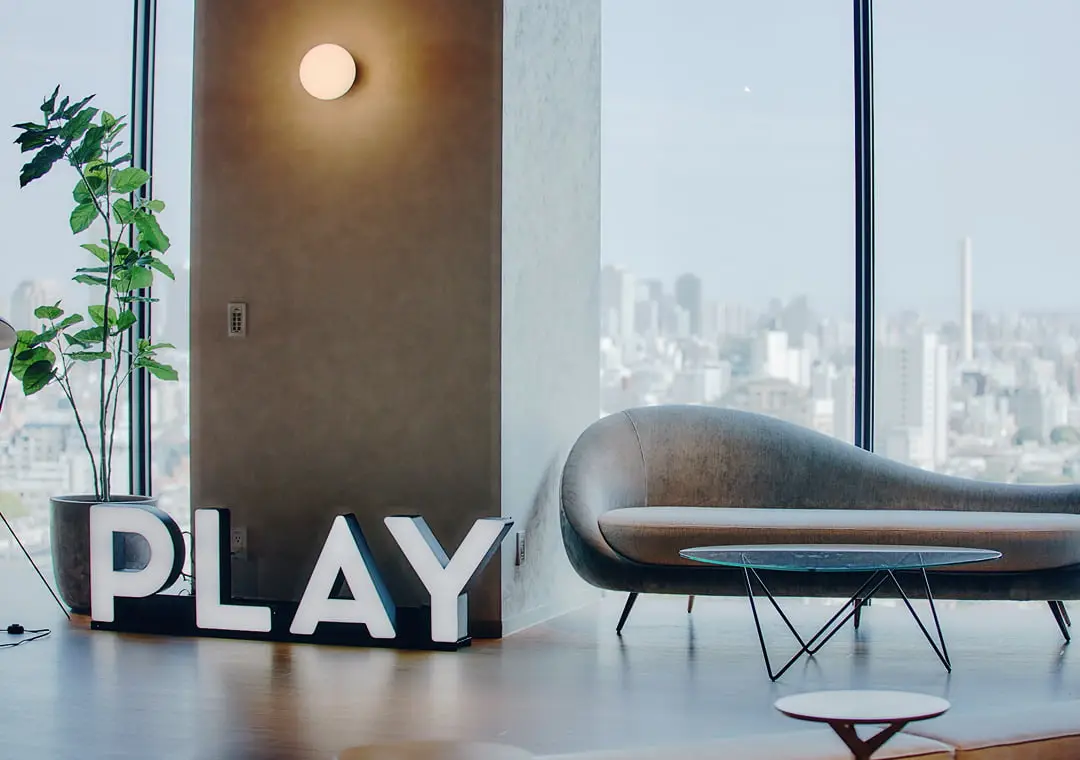 大きな窓から都市のスカイラインを望む、モダンなソファと「PLAY」の文字が飾られたスタイリッシュなラウンジ空間