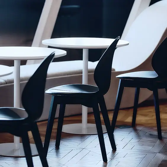 モダンなダークカラーの椅子と白い丸テーブルが並ぶ、寄木細工の床が特徴的なスタイリッシュなラウンジ空間