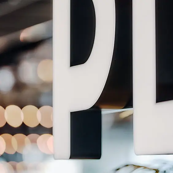 白い文字「P」のサインのクローズアップ、背景には暖色系のボケた光が広がる