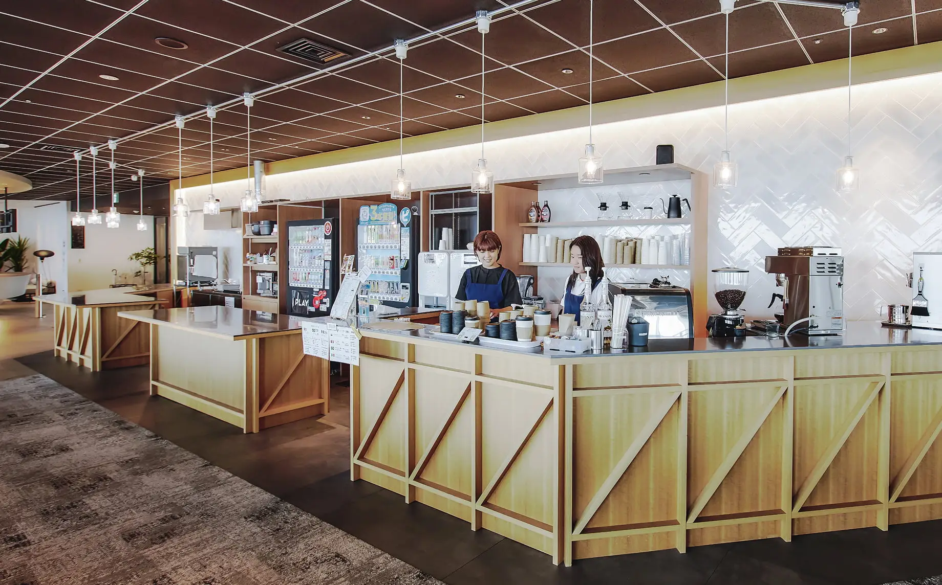 モダンな木製カウンターでコーヒーを提供する2人の女性バリスタがいる、明るく広々としたカフェスペース