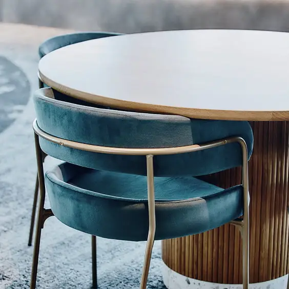 モダンな木製丸テーブルと、ティール色のベルベット製チェアが並ぶ洗練された空間