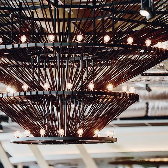 複数層のモダンなシャンデリア、ダークカラーの金属棒に多数の小さな電球が温かい光を放つ