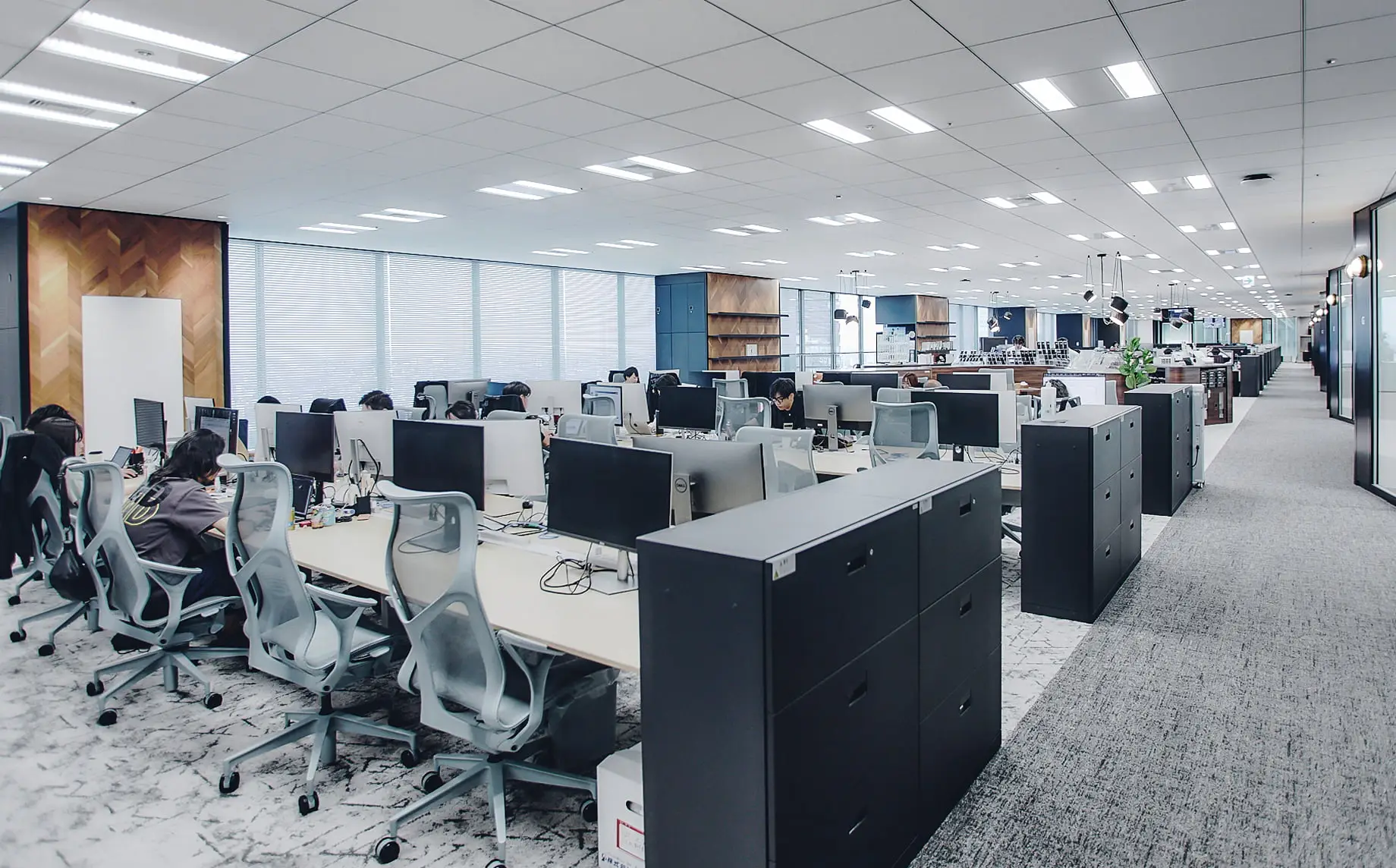 明るく照らされたモダンなオープンオフィスで、多くの従業員がワークステーションで作業している様子