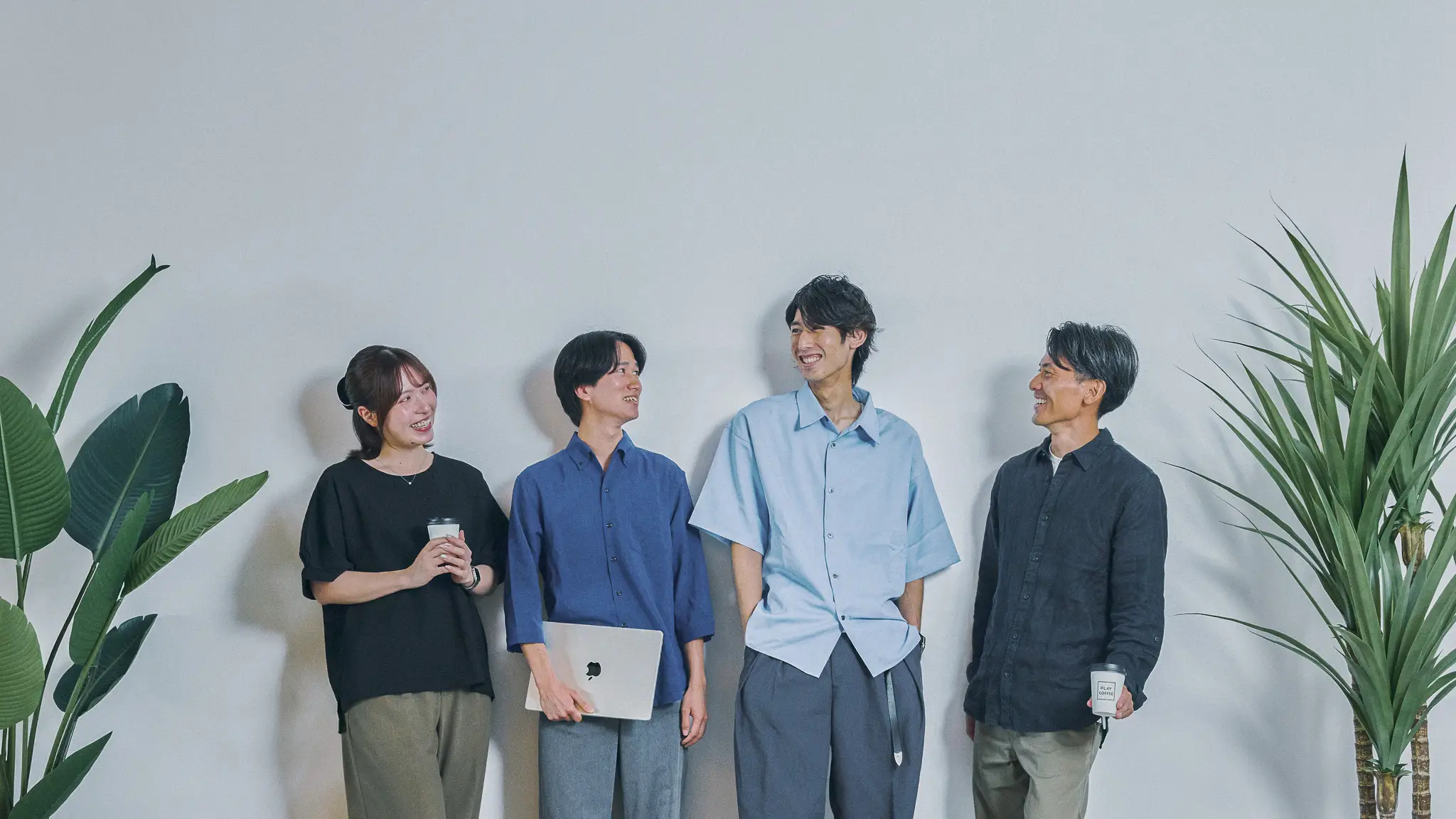 大きな窓から都市のスカイラインを望むモダンなオフィスで、3人の若いビジネスパーソンがノートパソコンを囲んで笑顔で共同作業をしている様子